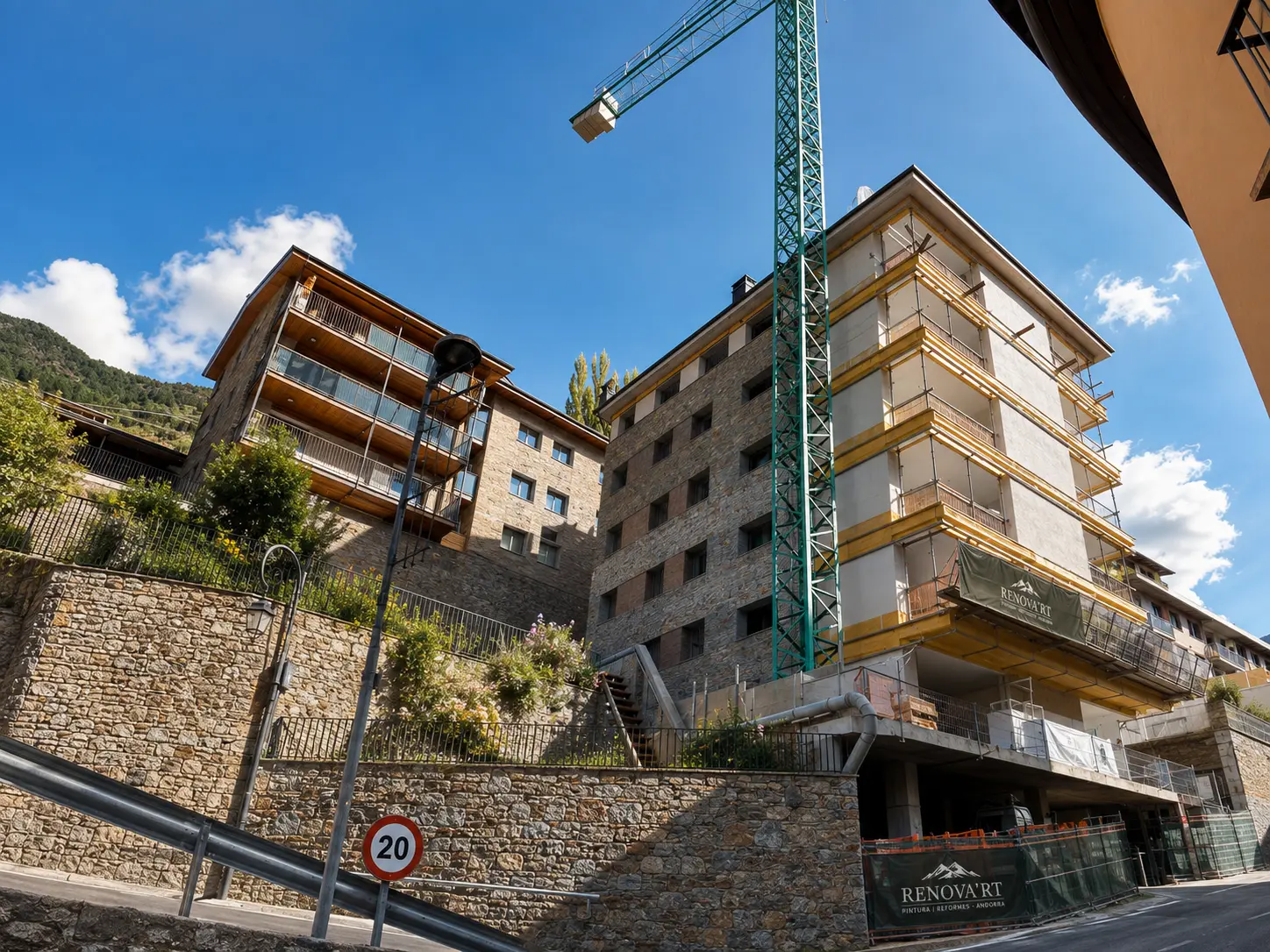 Edifici de pedra en rehabilitació amb grua, bastides i lona de Renova'rt a Andorra
