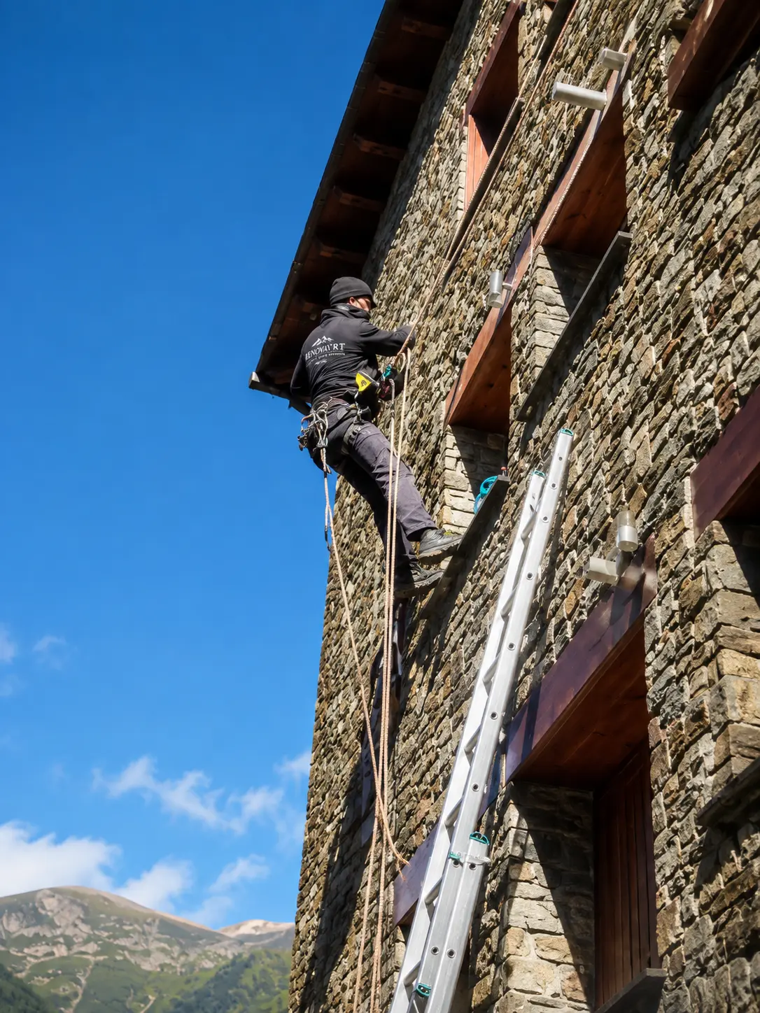 Treballador de Renova'rt suspès amb cordes fent treballs verticals en una façana de pedra a Andorra